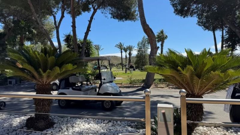 Golfbilar vid golfbanan El Plant�o i Alicante, omgivna av palmer och gr�nska.